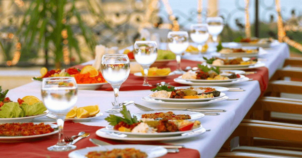 Outdoor catering table with plates, glasses, and food for events.
